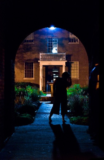 Night photo, barefoot figure silhouetted under brick archway in lit courtyard, likely exercise source still