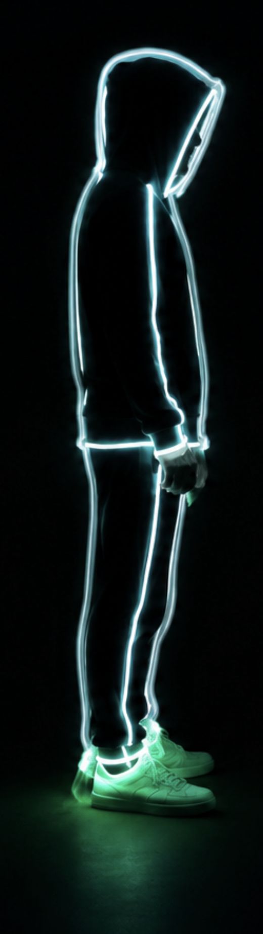 Side profile of the glowing wireframe figure, hood up, hands visible near the waist.