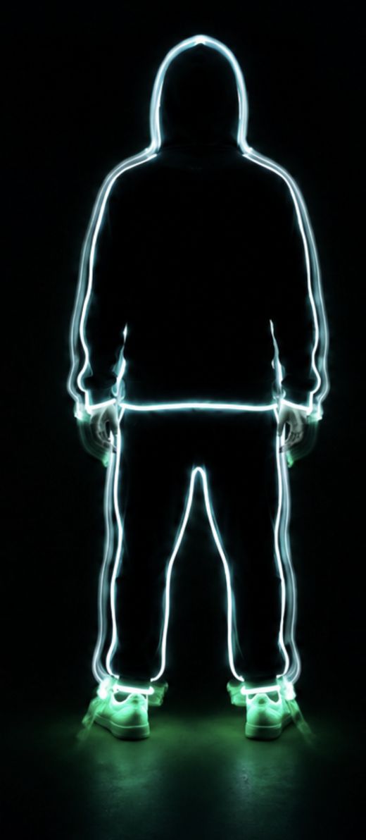 Back view of the glowing wireframe figure, smooth rounded hood, green-glowing sneakers visible at the feet.